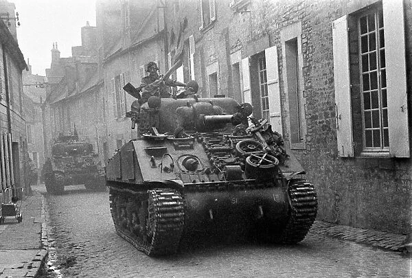 British troops in Sherman tanks roll throught the narrow cobbled streets of a Normandy