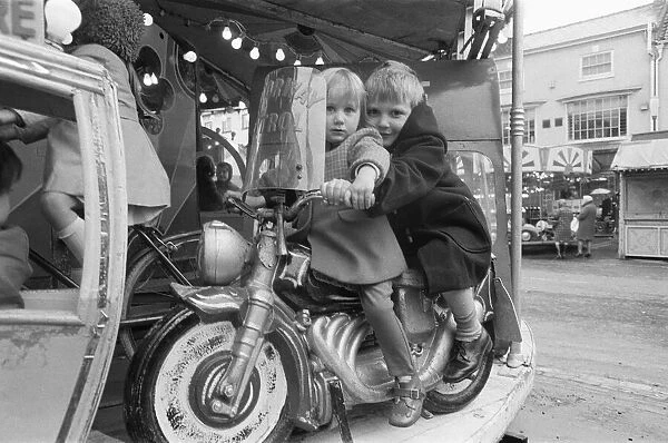 Brother and sister riding a motorcycle on a childs roundabout at the Northallerton