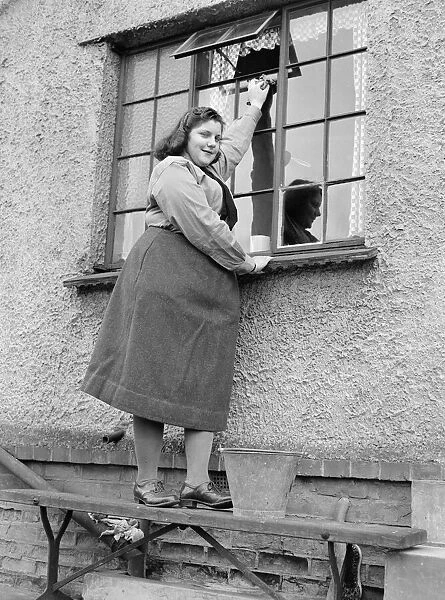 A busy housewife cleaning her windows at home Circa 1954