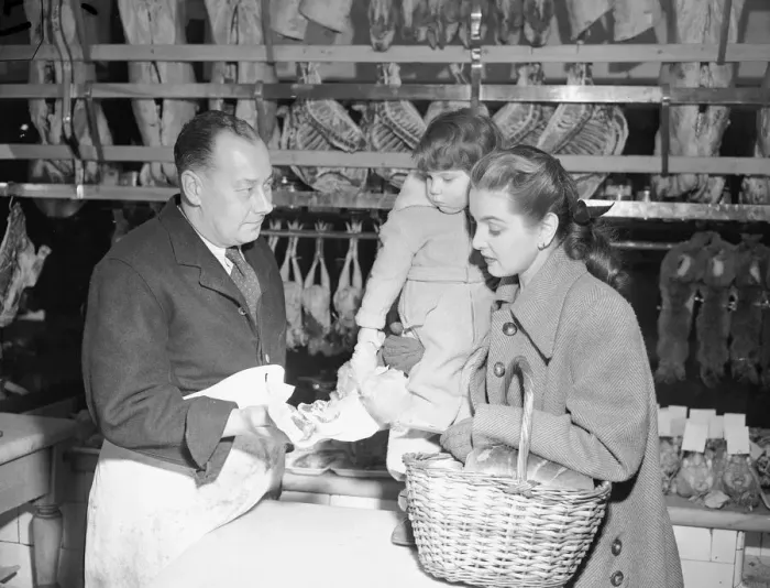 Framed Print : Butcher offers choice cuts of meat to a woman shopper March 1952