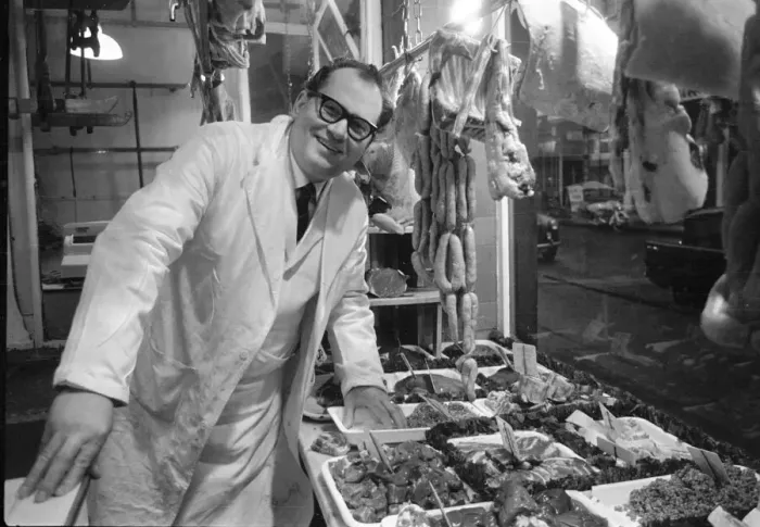 Framed Print : Butcher stands proudly in his shop as his various meat products are displayed in window Framed Print : Butcher stands proudly in his shop as his various meat products are displayed in window