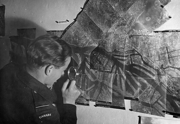 A Canadian Photographic Reconnaissance pilot examines a picture of Hamburg