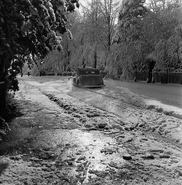 Car drives along a road covered in deep snow in Tadworth. April 1950 O23770-007
