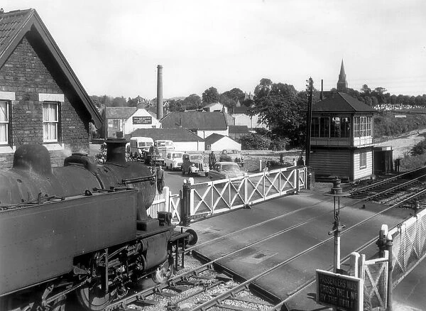 Cars queue as a local train crosses the level crossing at Warmley in 1960