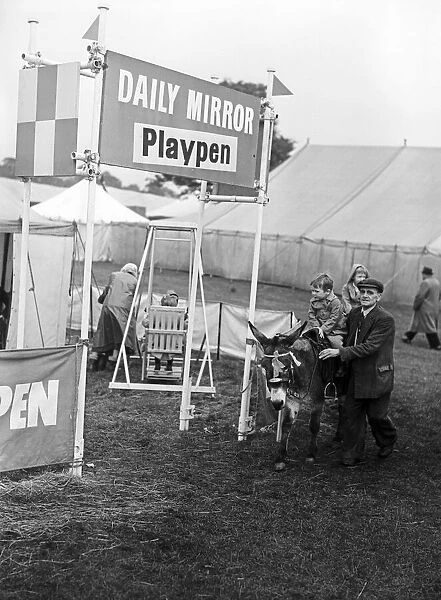 A child riding on a donkey past the Daily Mirror Playpen at Altrincham agriculture show