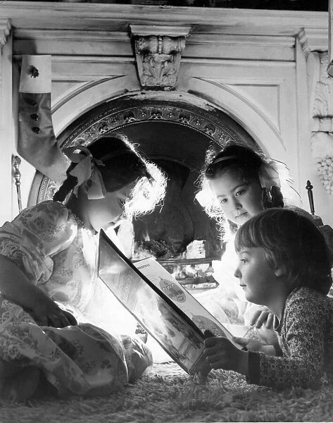 Three children listen to a fairytale in front of roaring fire at Christmas time