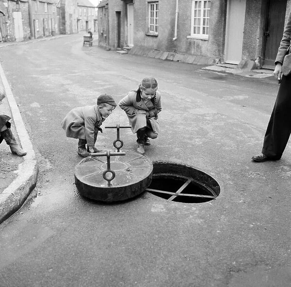 Children looking down a drain hole in the road in Thornbury, South Gloucestershire