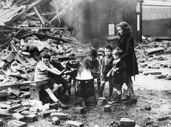 Children in a Manchester suburb warm themselves by a fire outside wrecked houses during