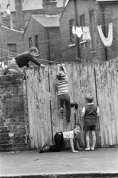Children playing in the streets, climbing a fence. June 1964