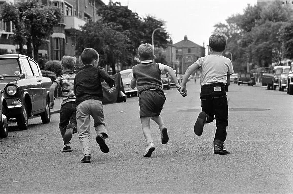 Children playing in the streets, running down the road. June 1964