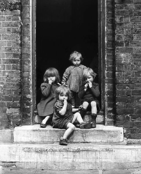 Children sitting in a doorway left behind in bombed out Doris Street, Lambeth, London