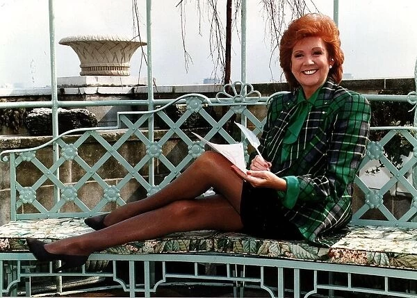 Cilla Black television presenter writing with feather legs streched along bench green