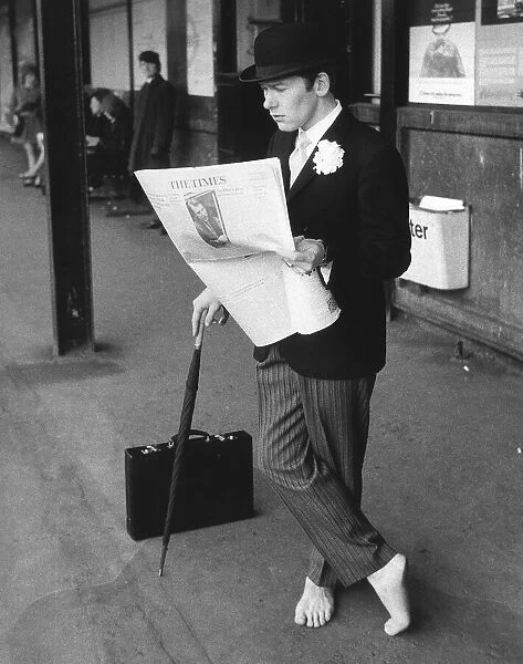 A city gent dressed in pin stripes, bowler hat and leaning on a brolley reads his copy of