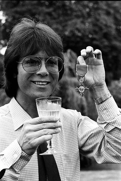 Cliff Richard with his OBE medal award drinkng wine 1980