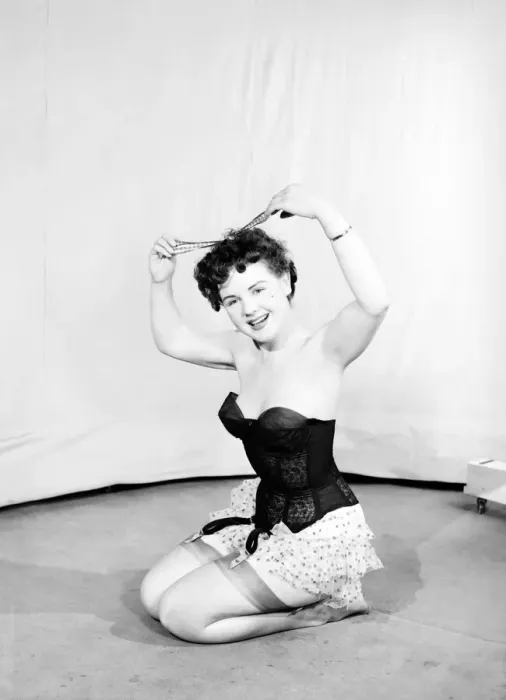 Framed Print : Clothing: Fashion: Underwear: Woman wearing corsett placing bow in hair. 1959