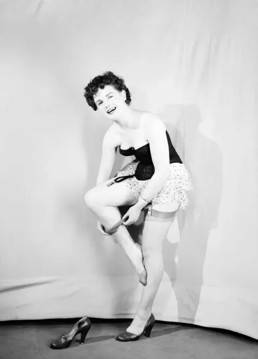 Framed Print : Clothing: Fashion: Underwear: Woman wearing corsett placing bow in hair. 1959
