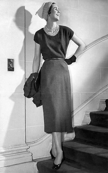 Clothing. Model wears calf-length dress, gloves, hat and necklace standing on stairs