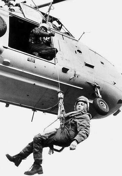 A Coastal Guards is lowered down from a helicopter on a winch to come to someone