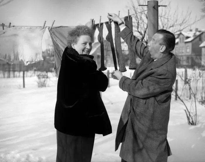 Framed Print : A couple hanging out their washing - socks, smiling in the snow 8th January 1955 Framed Print : A couple hanging out their washing - socks, smiling in the snow 8th January 1955