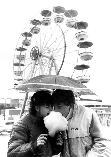 Couple sharing candyfloss under an unmbrella in a wet Southend. 8th April 1985