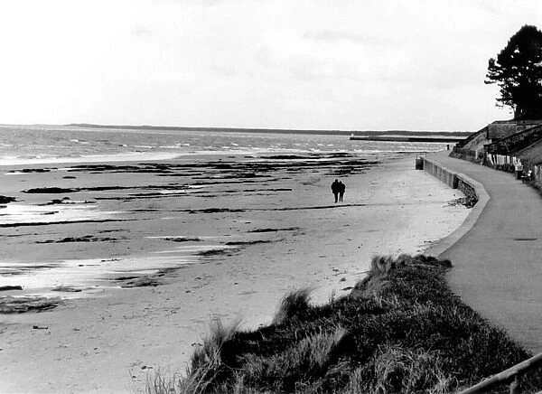 A couple take a stroll along Nairn beach in Scotland. Circa 1970