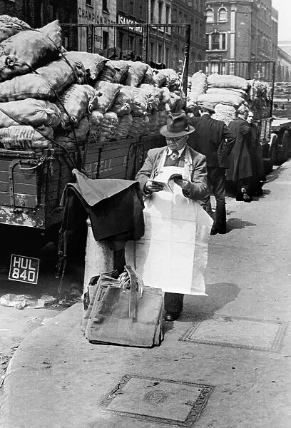 Covent Garden Market stall vendor stops to read a magazine. Circa 1955