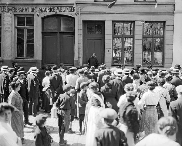 A crowd gather outside a house being searched for German spies by the police