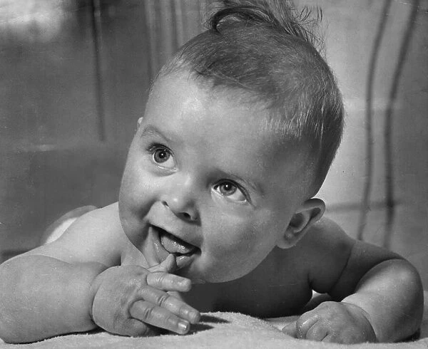 Cute baby sucking on his thumb and smiling February 1959