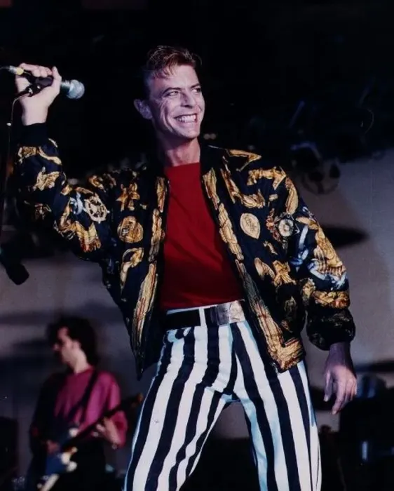 : David Bowie singer on stage mike in hand wearing black and white striped trousers red : David Bowie singer on stage mike in hand wearing black and white striped trousers red