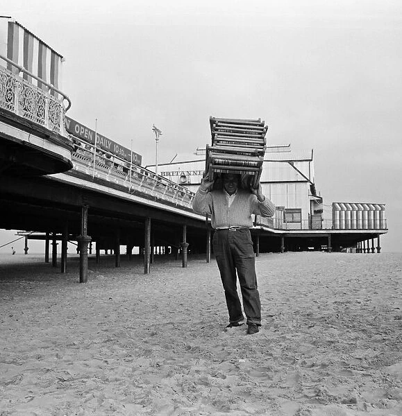 A deck chair attendant carrying deck chairs on his head. Great Yarmouth, Norfolk