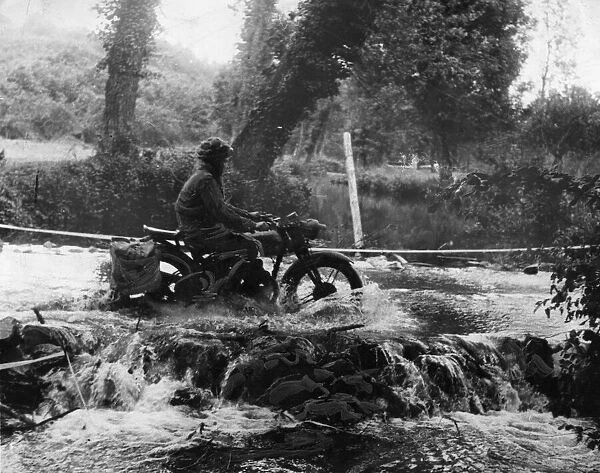 A despatch rider splashes through a ford to the cross the river in the Odon Valley in