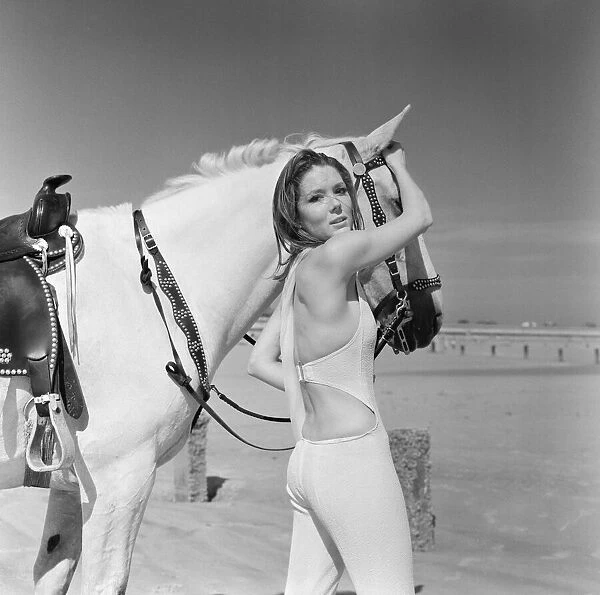 Diana Rigg, who plays Emma Peel, looking serious to camera with a white horse