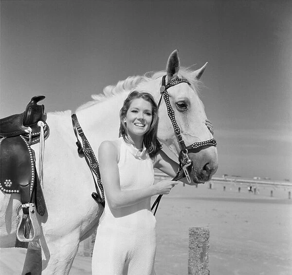 Diana Rigg, who plays Emma Peel, smiling with a white horse on the beach at St Mary