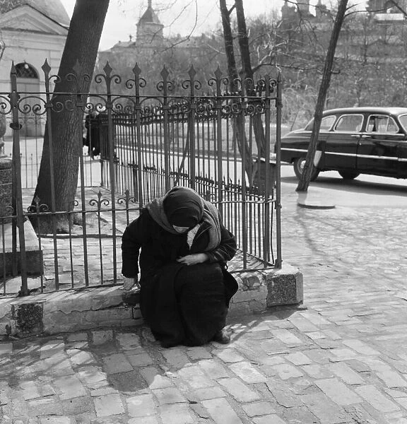 An elderly female resident of the Soviet city of Kiev, sitting on a low wall in one of