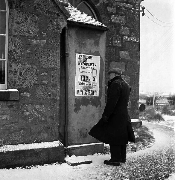 An elderly man reading a notice put up on the wall of his local church in Scalloway