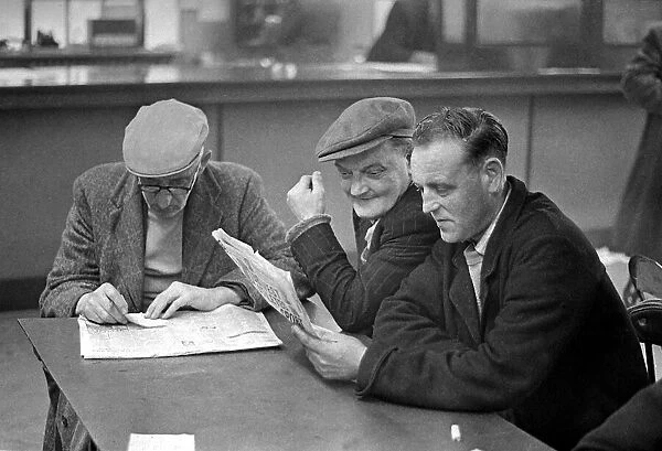 Elderly men study the form guide before placing their bet in a betting shop