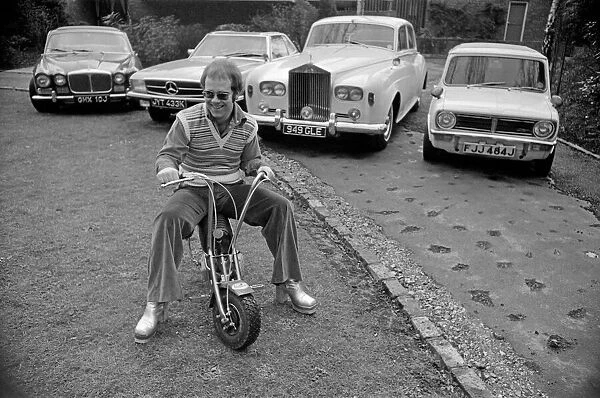 Elton John pictured at his home, sitting on a small motorbike in front of four of his