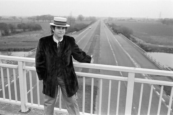 Elton John pictured standing on a bridge over the motorway. 5th December 1982