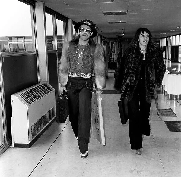 Elton john singer arriving at heathrow airport in1974 with un-named woman wearing fur