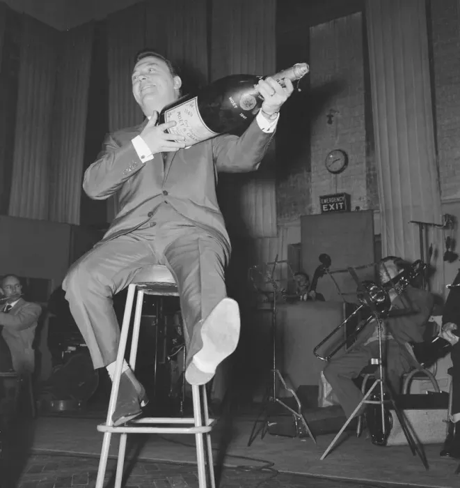 Framed Print : English singer Matt Monro with a giant size bottle of champagne as he works on his latest Framed Print : English singer Matt Monro with a giant size bottle of champagne as he works on his latest