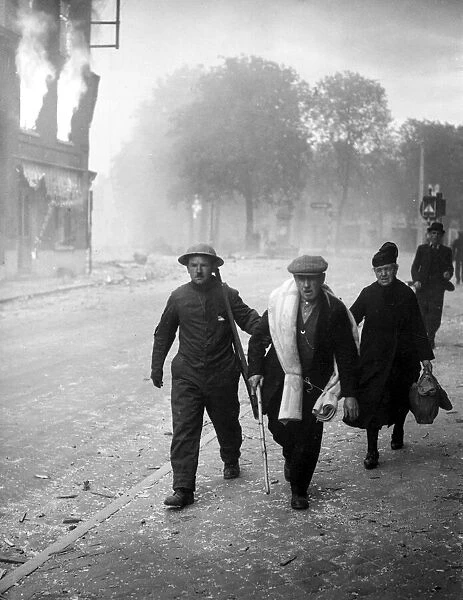 An English soldier helps some refugees through a burning town in Belgium following German