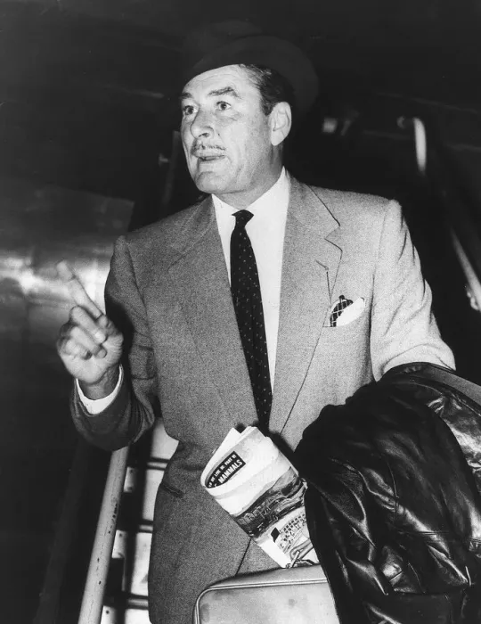 Framed Print : Errol Flynn pointing his finger and holding a suitcase and a news paper with a black