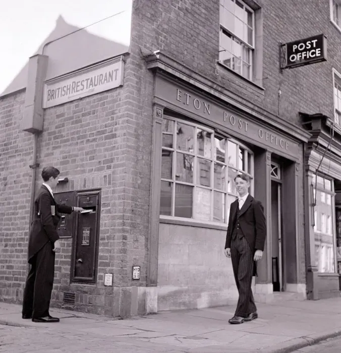 Framed Print : Eton schoolboy walks past Eton Post Office whilst another boy posts a letter dressed in