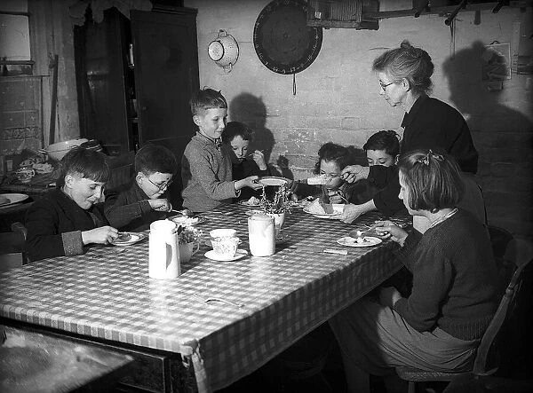 Evacuees with women voluntary service helper sitting at table eating food during WW2