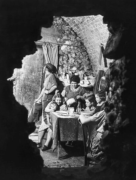 A family eating dinner in the bombed out remains of their cellar. October 1940