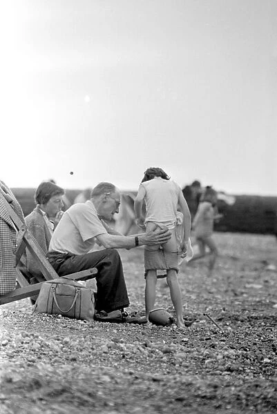 Family help a young boy to get changed as they sit on their deckchairs on the beach at