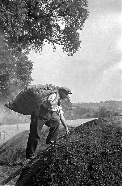 A farmer climbing a mound of soil carrying with him a sack on a farm in England