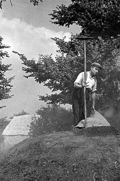 A farmer standing on top of a mound of peat circa 1938