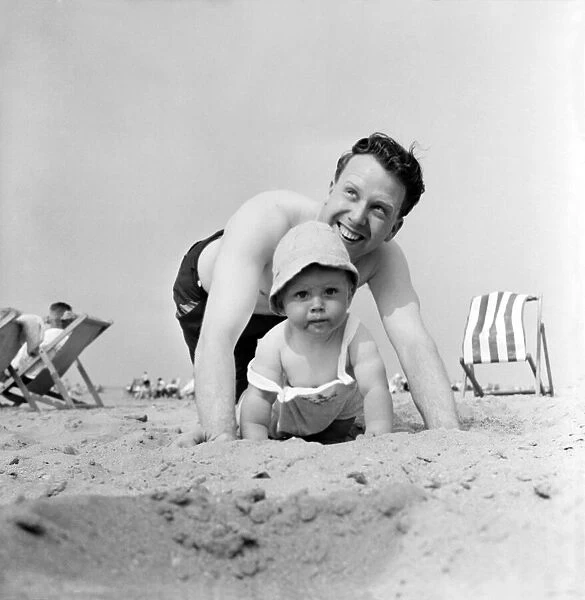 Father and child playing on the beach during a hot summer day in Britain June 1960