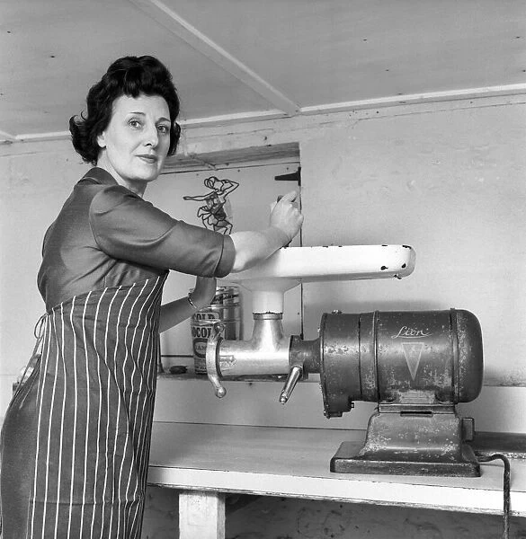 A female butcher seen here at work in her shop, using the mincer. 1963